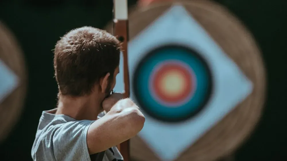 An archer at full draw with a recurve, facing a target at the range